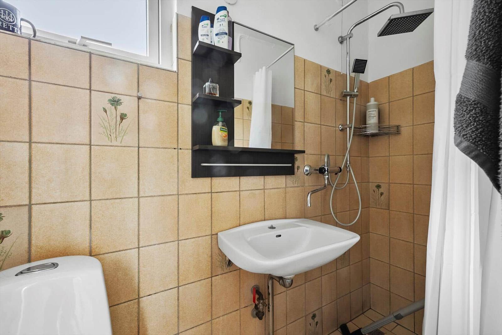 Badezimmer mit Dusche, Waschbecken und Toilette. Wandfliesen mit Blumenmotiv.