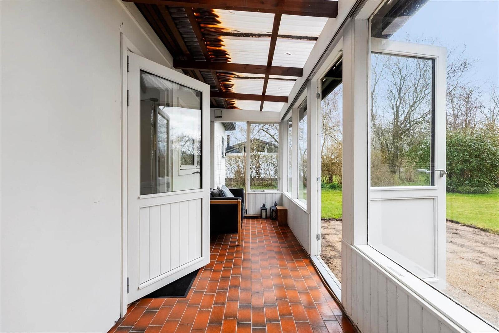 Terrasse mit roten Fliesen und Glasfronten führt zu einem Sitzbereich.