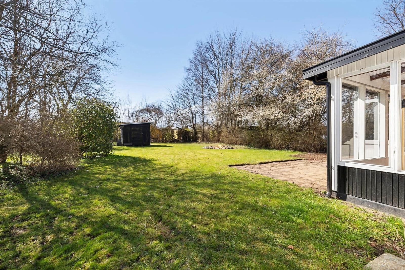 Grüner Garten mit Holzhaus und blühenden Bäumen im Hintergrund.