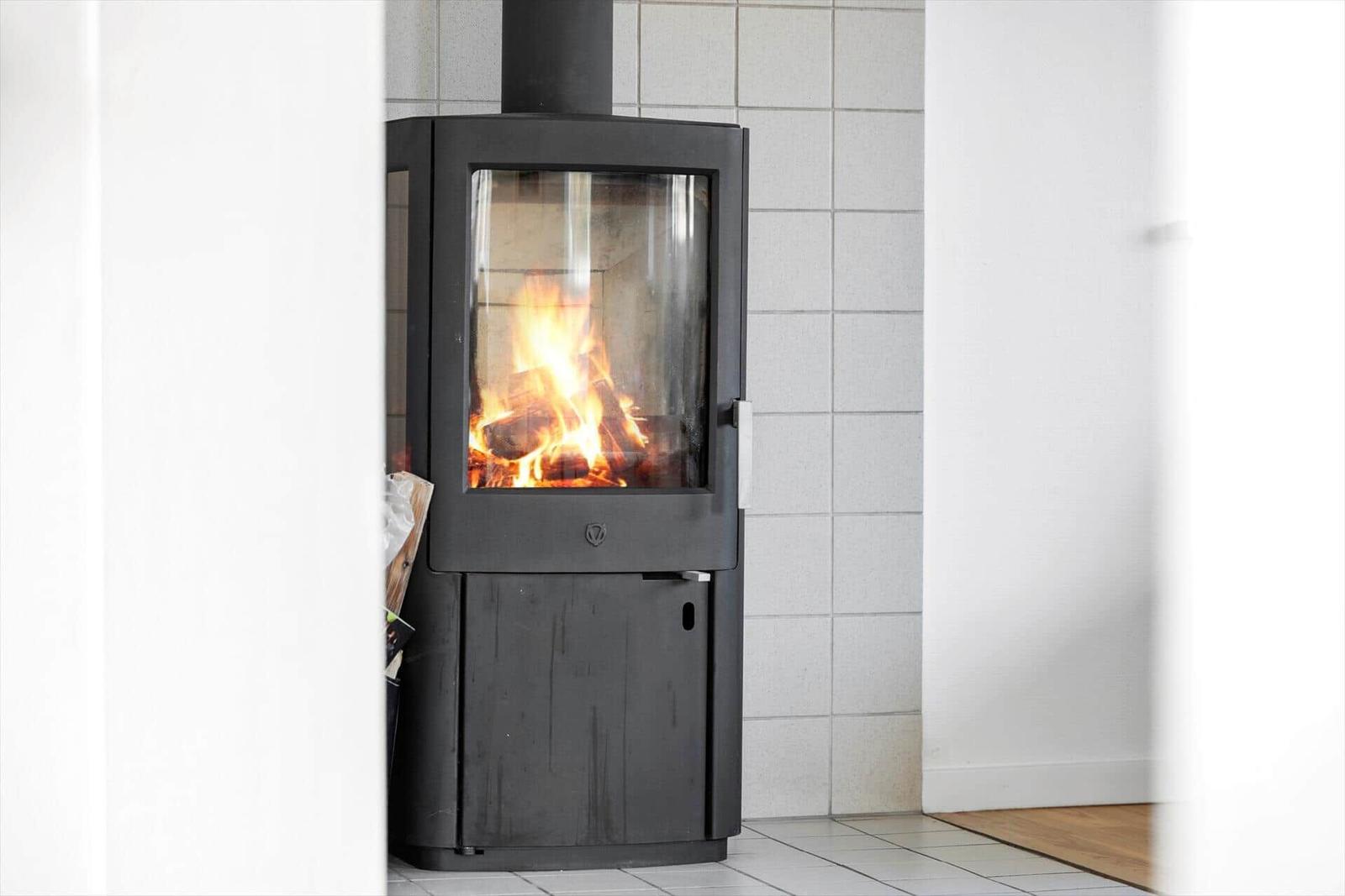 Kaminofen mit brennendem Holz in einem Raum mit weißen Wänden und Fliesenboden.