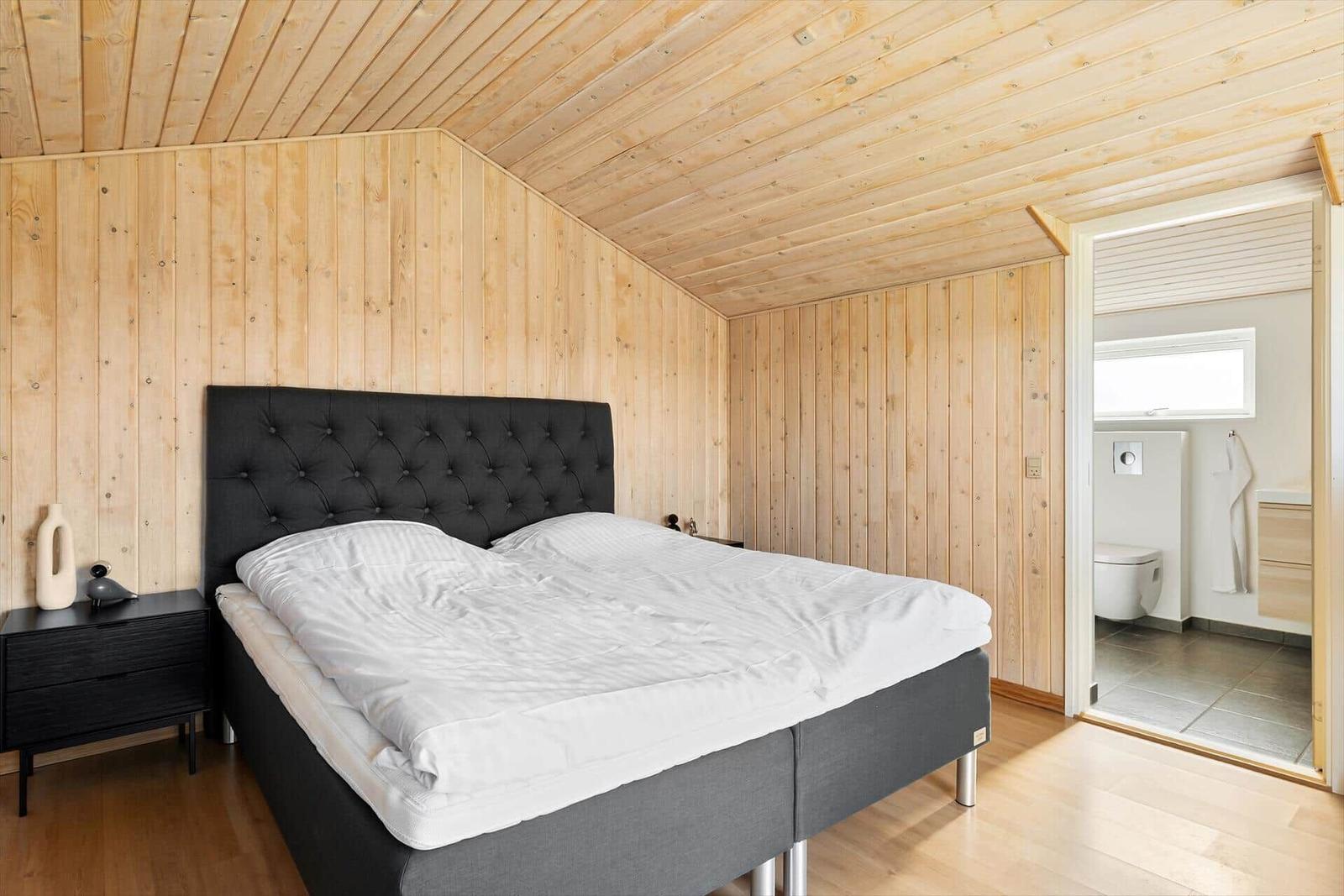Schlafzimmer mit Holzwand und Bett. Nebenraum mit Toilette.