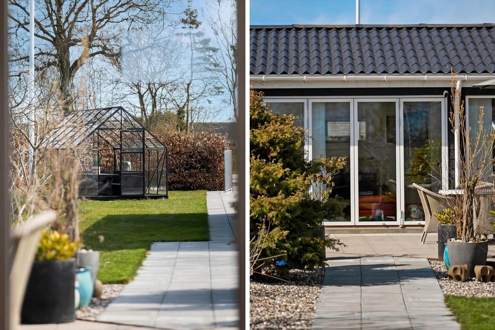 Garten mit Gewächshaus und Terrasse mit Sitzgelegenheiten. Modernes Haus mit Glasfront.