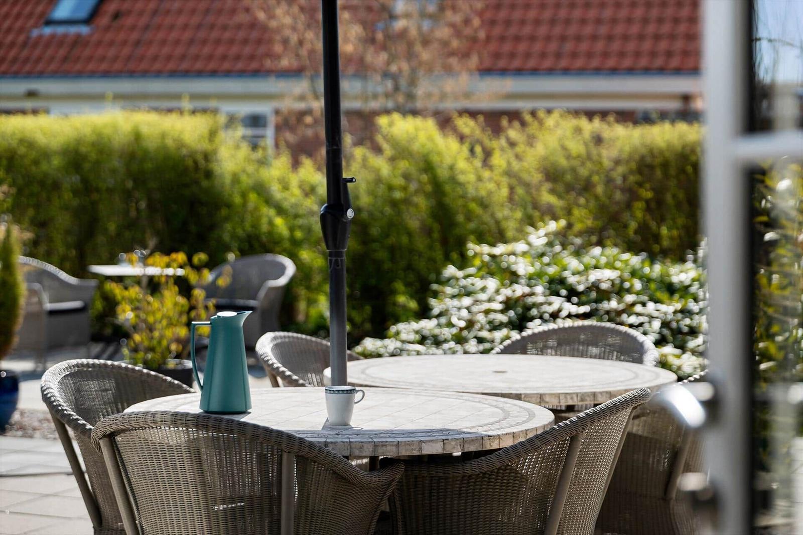 Terrasse mit Tisch, Stühlen und Kaffeetasse. Hintergrund: grüne Hecke und Haus.
