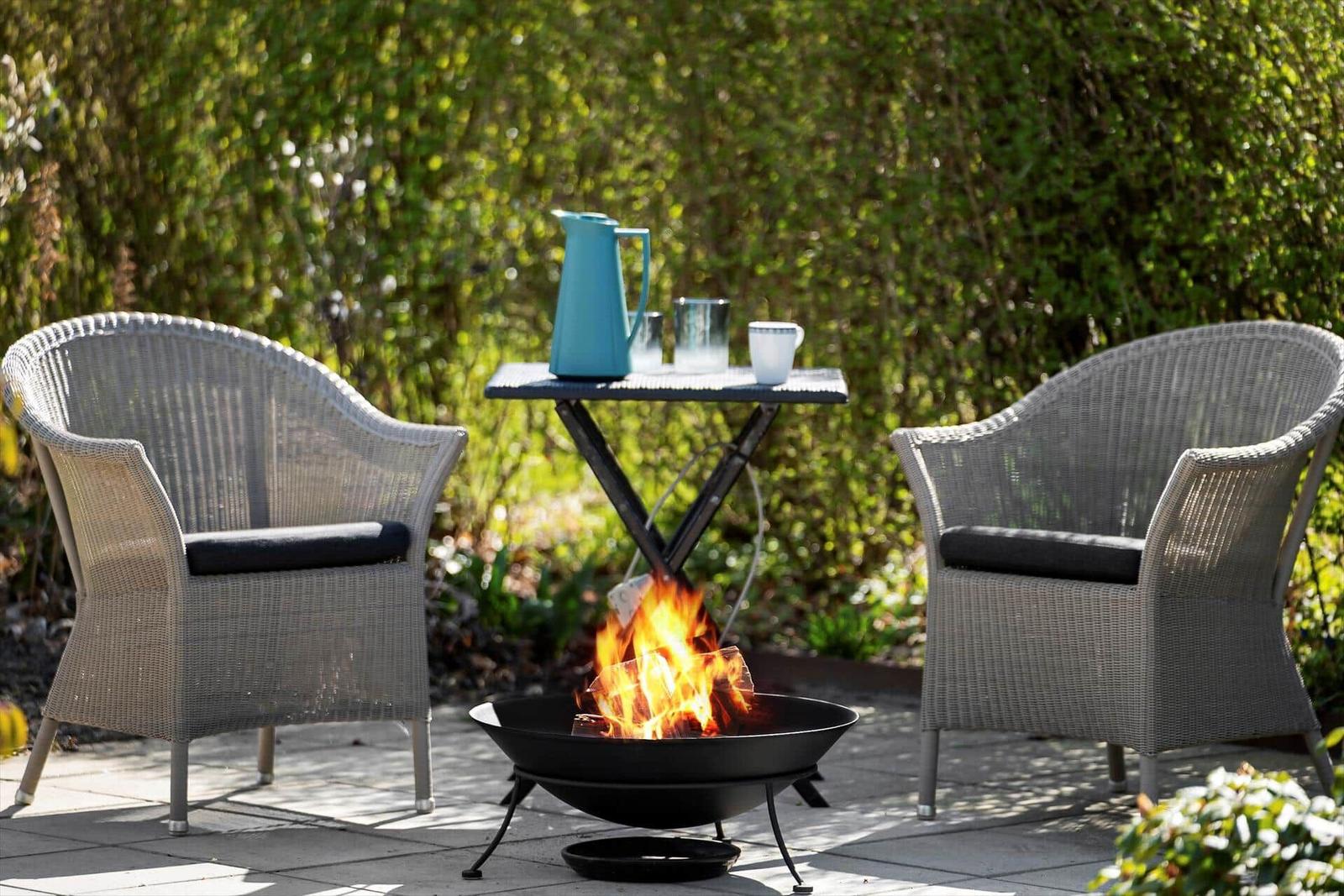 Zwei Stühle und ein Tisch um einen brennenden Feuerkessel im Garten.