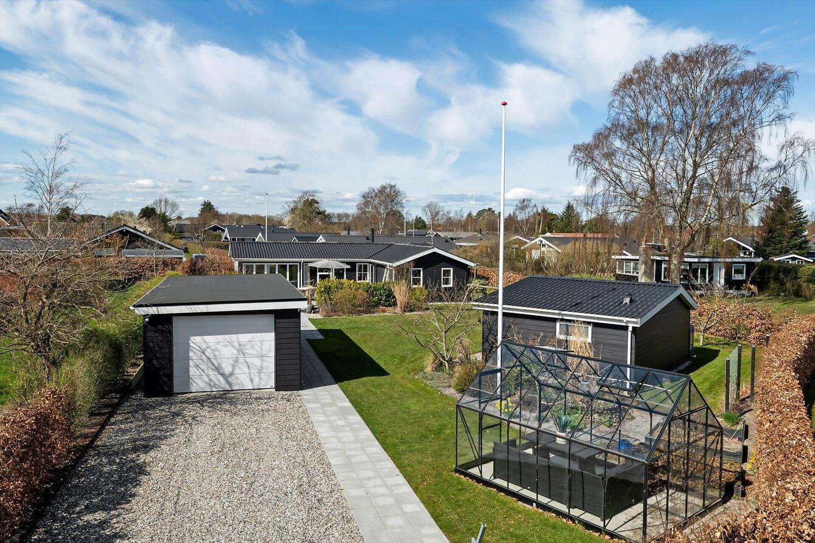 Modernes Haus mit Garage, Gewächshaus und Garten. Blick auf Wohnhaus und Umgebung.