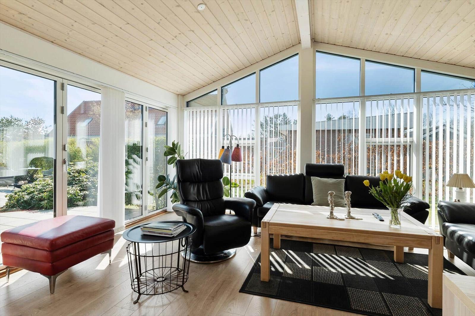 Wohnzimmer mit schwarzer Ledermöbeln, Holzfußboden und großen Fenstern.