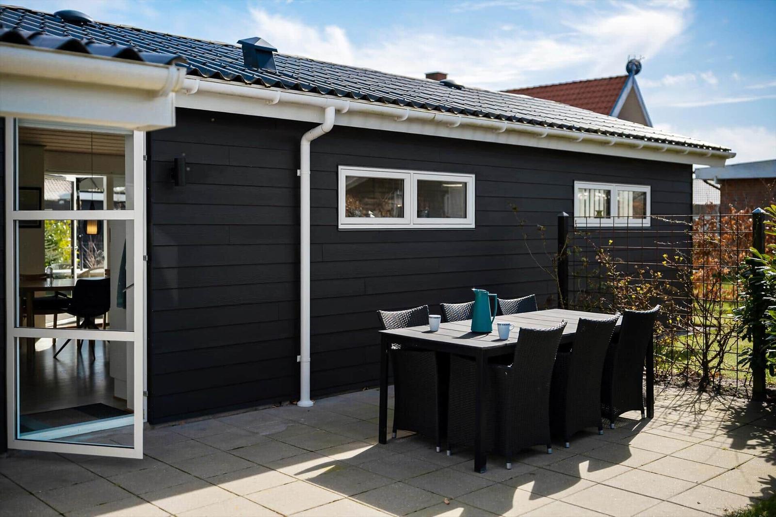 Schwarzes Haus mit Terrasse und Sitzgruppe. Glastür führt ins Innere.