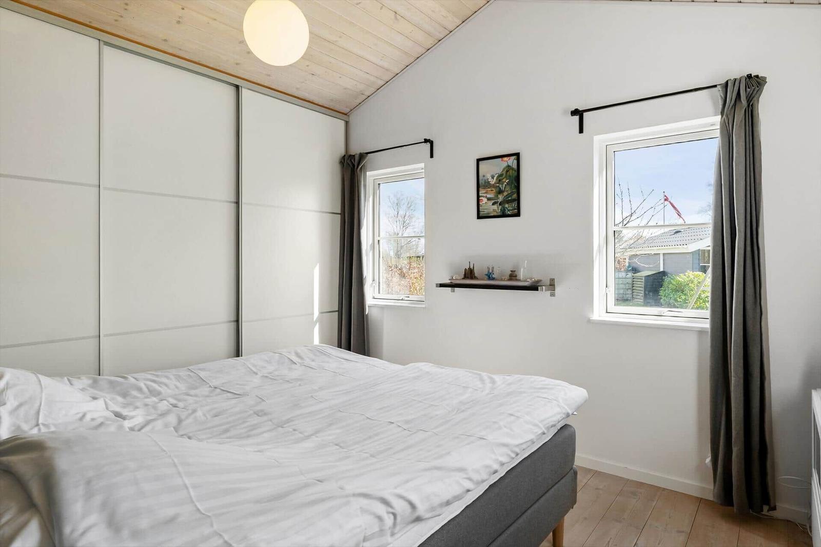 Schlafzimmer mit Bett, Fenstern und Schiebetüren.