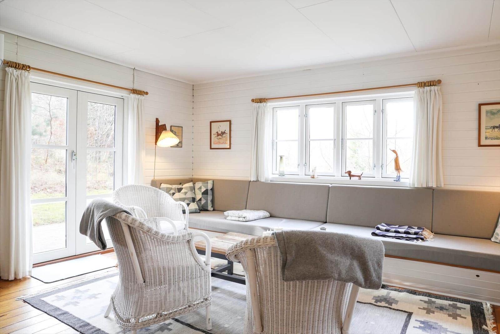Wohnzimmer mit Sofa, zwei Stühlen und Fenstern mit Blick nach draußen.