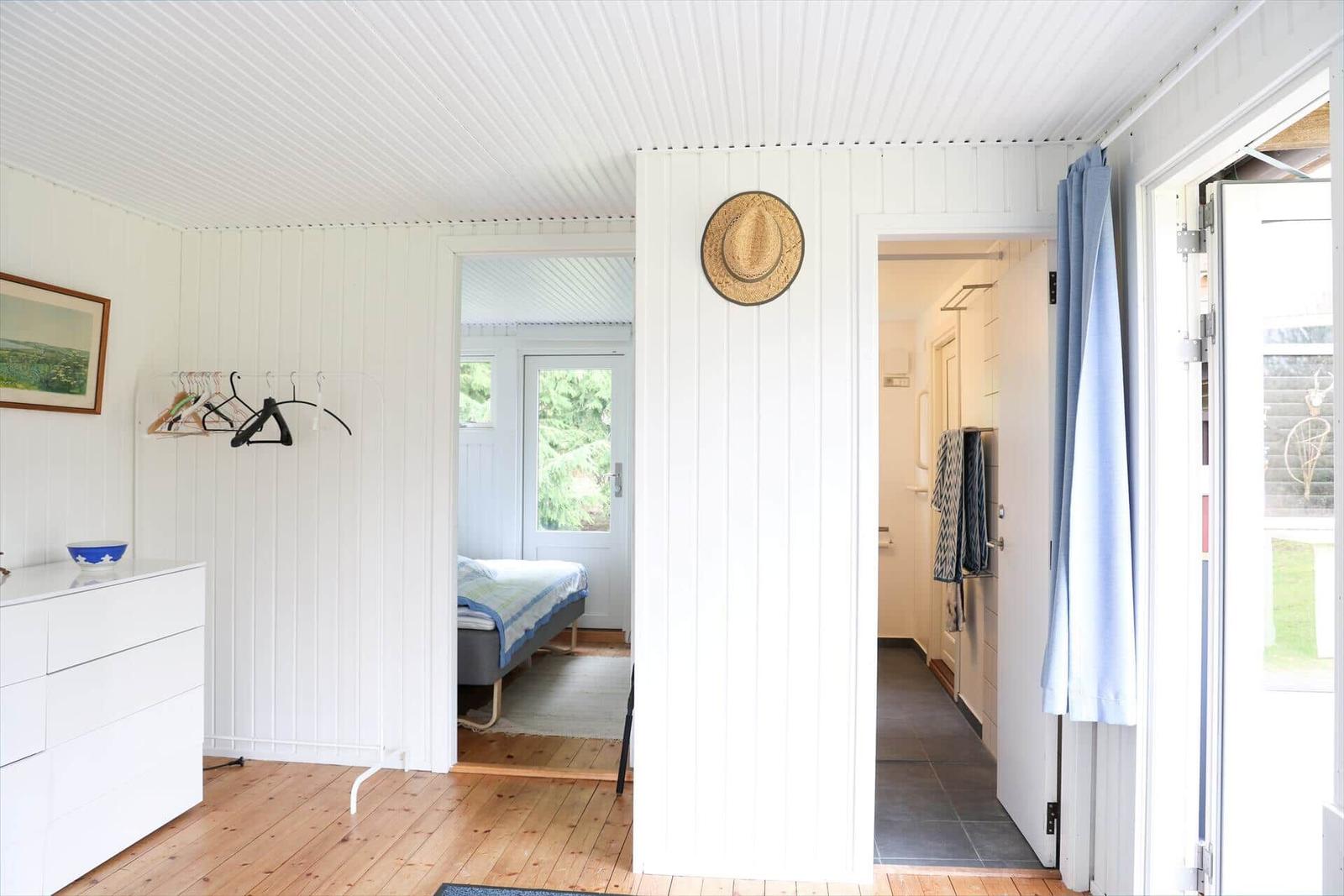 Wohnraum mit Schlafzimmer und Bad. Holzboden, weiße Wände und Tür. Hut an Wand.
