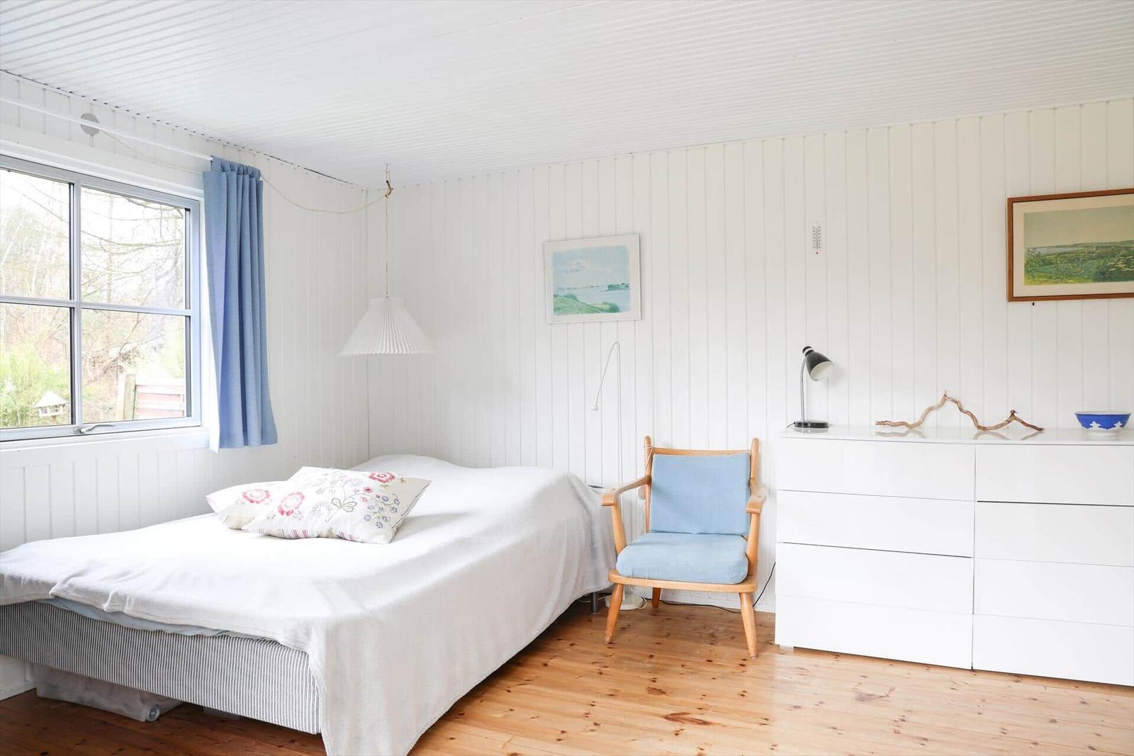 Schlafzimmer mit Bett, Stuhl und Schrank an weißer Wand.