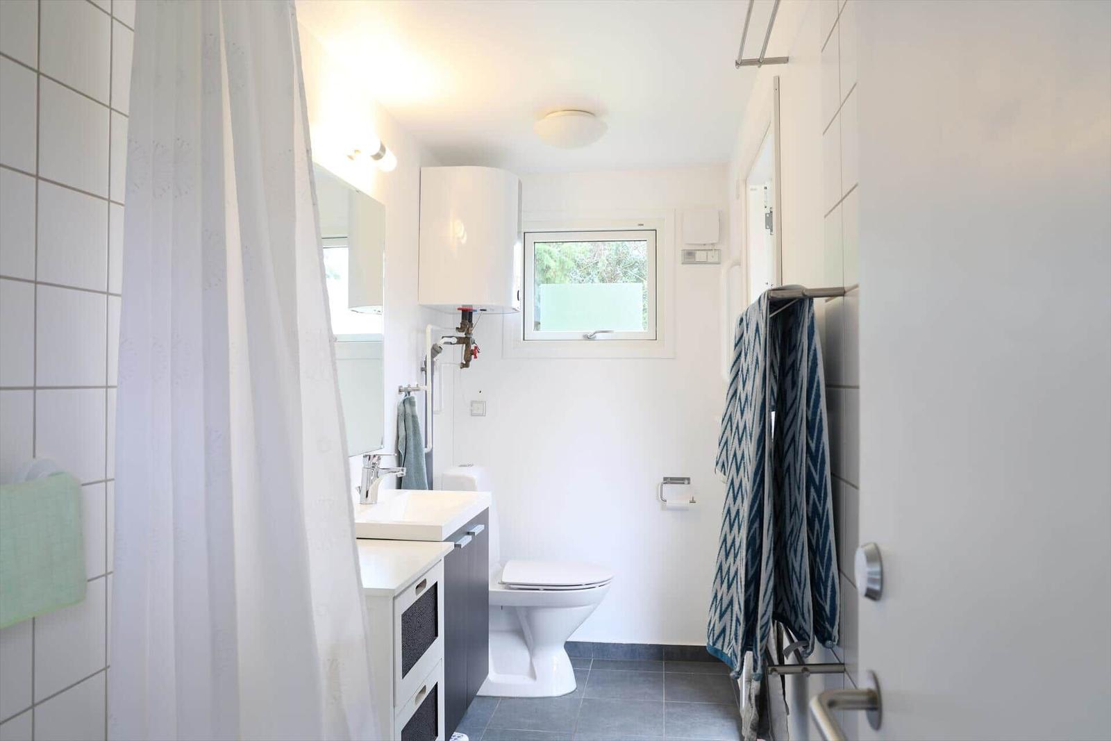 Badezimmer mit Toilette, Waschbecken und Dusche. Fenster, Handtücher und Heizung sichtbar.