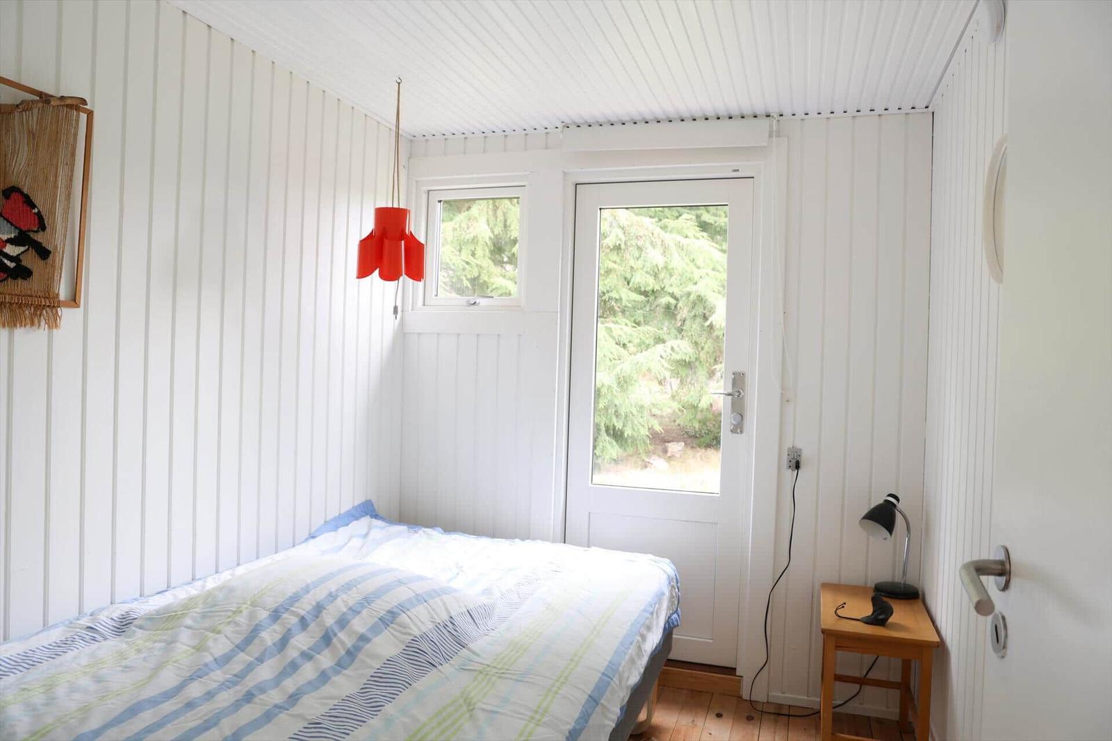 Schlafzimmer mit Bett, Fenster und Tür zur Außenseite.