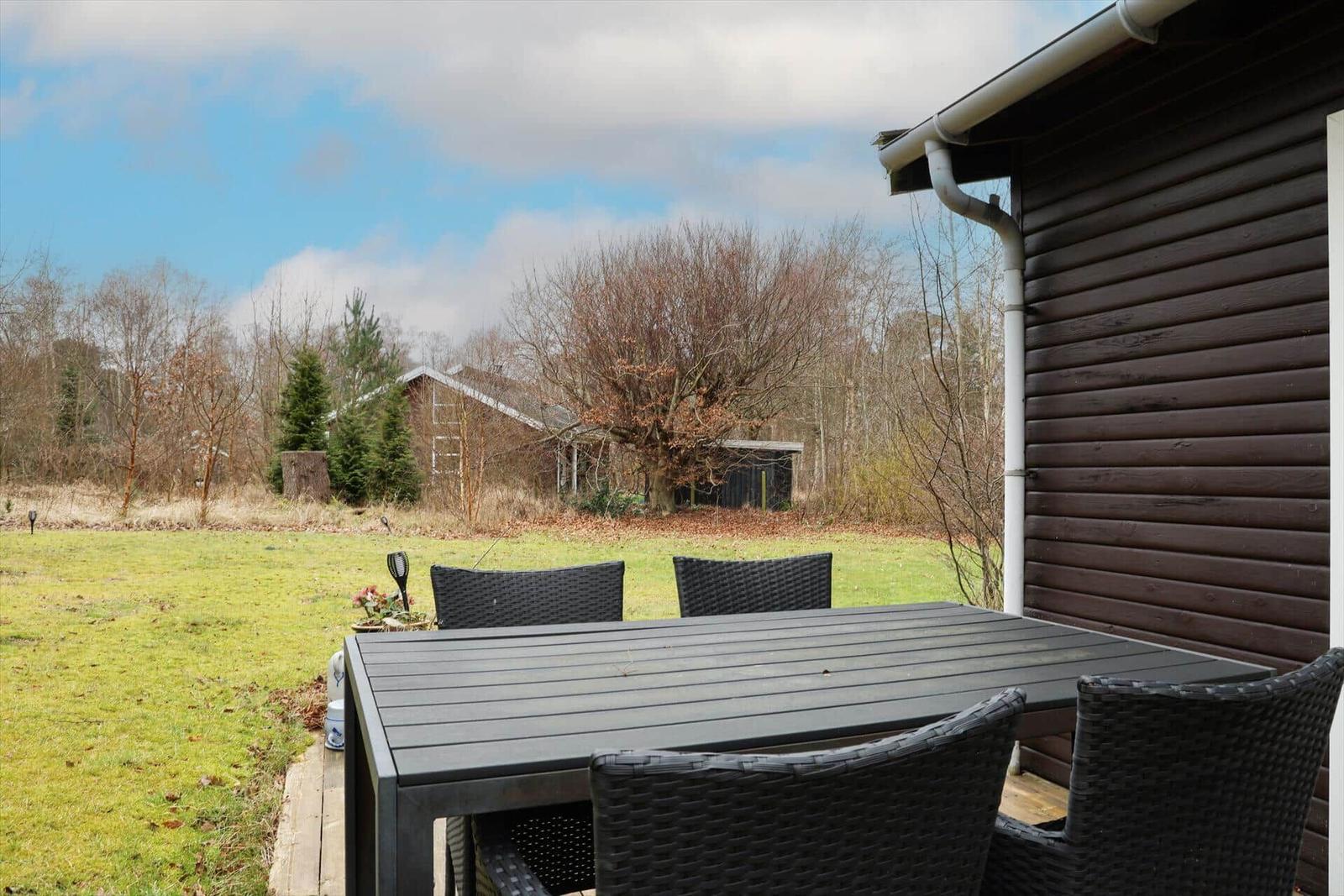 Terrasse mit Tisch und Stühlen, Blick auf grünen Rasen und Wald.