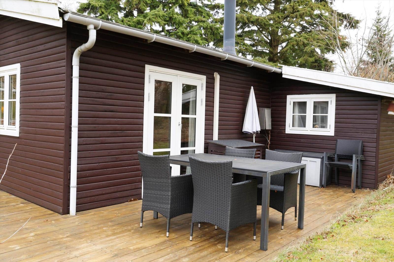 Terrasse mit Tisch und Stühlen vor einem Holzhaus mit weißen Fenstern.