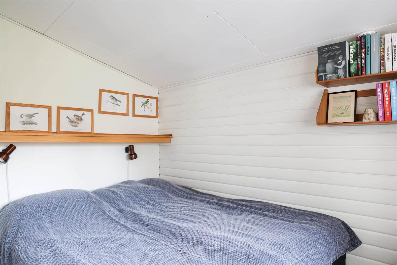 Schlafzimmer mit Bett, Wandregalen und Vogelbildern an der Wand.
