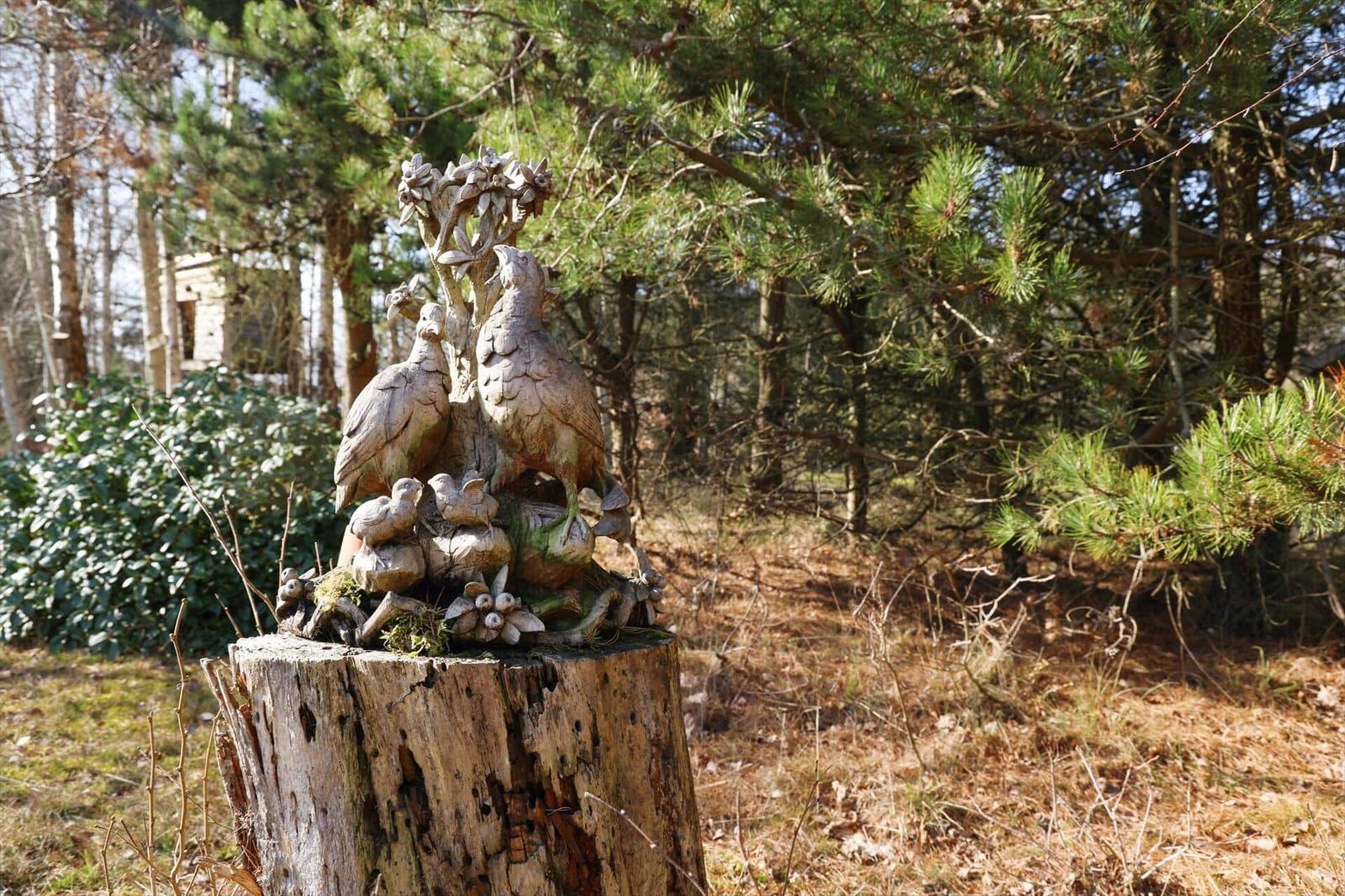 Holzschnitzerei auf Stumpf im Wald mit Vögeln und Blumen