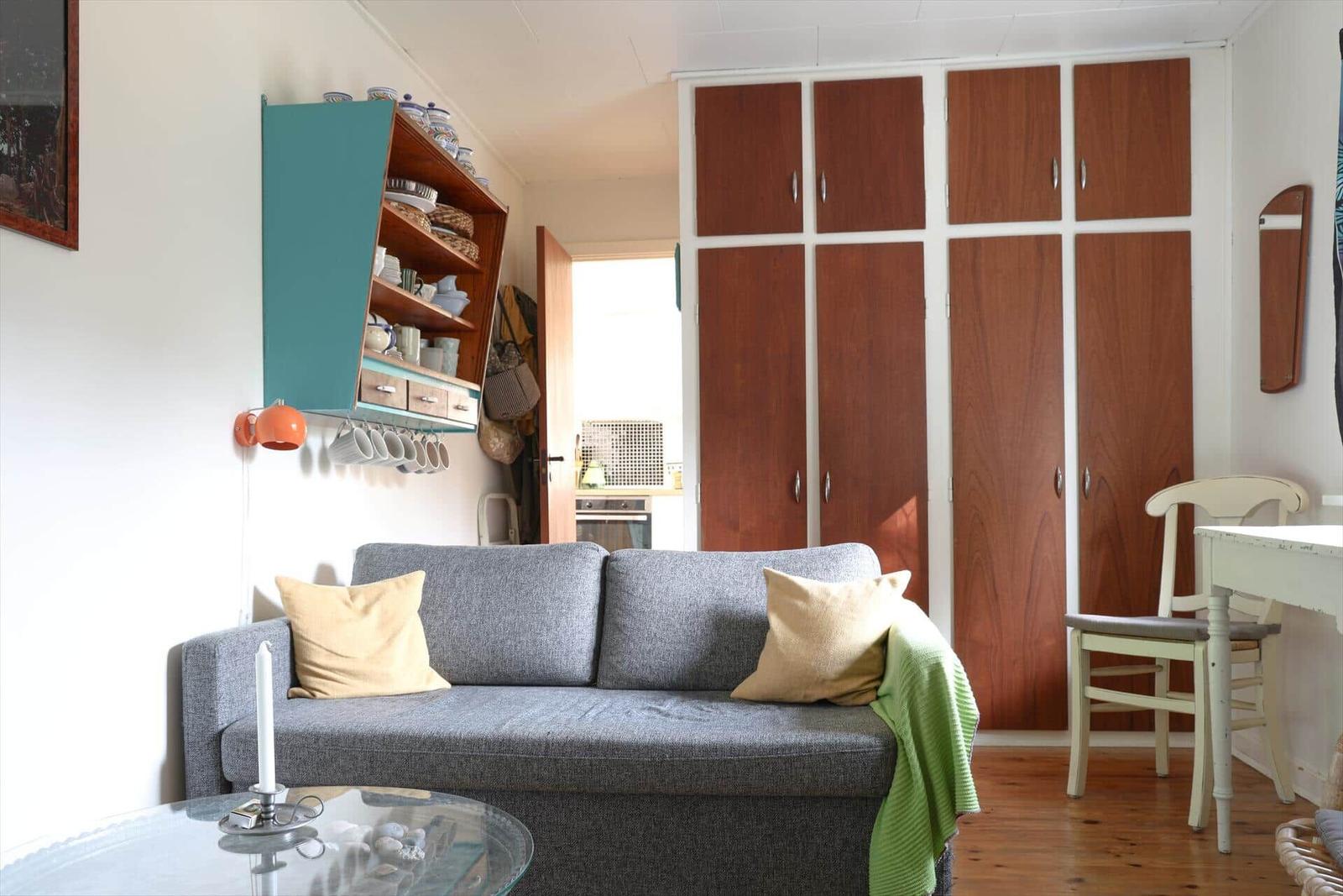 Wohnbereich mit Sofa, Küchenzeile und Holzschrank. Tisch und Stuhl sind vorhanden.