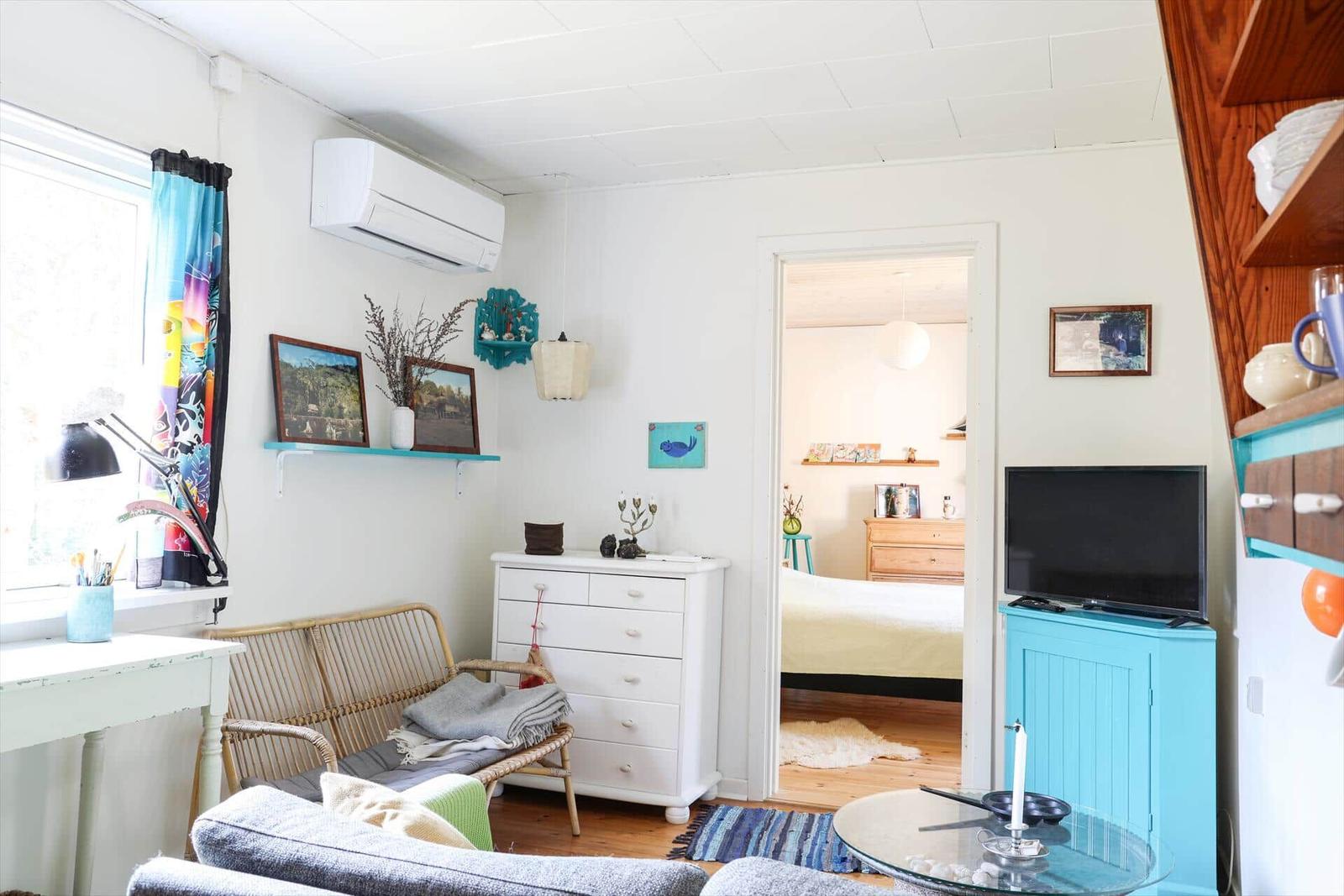 Wohnzimmer mit Sofa, Schreibtisch und TV. Durchgang zur Schlafzimmer.