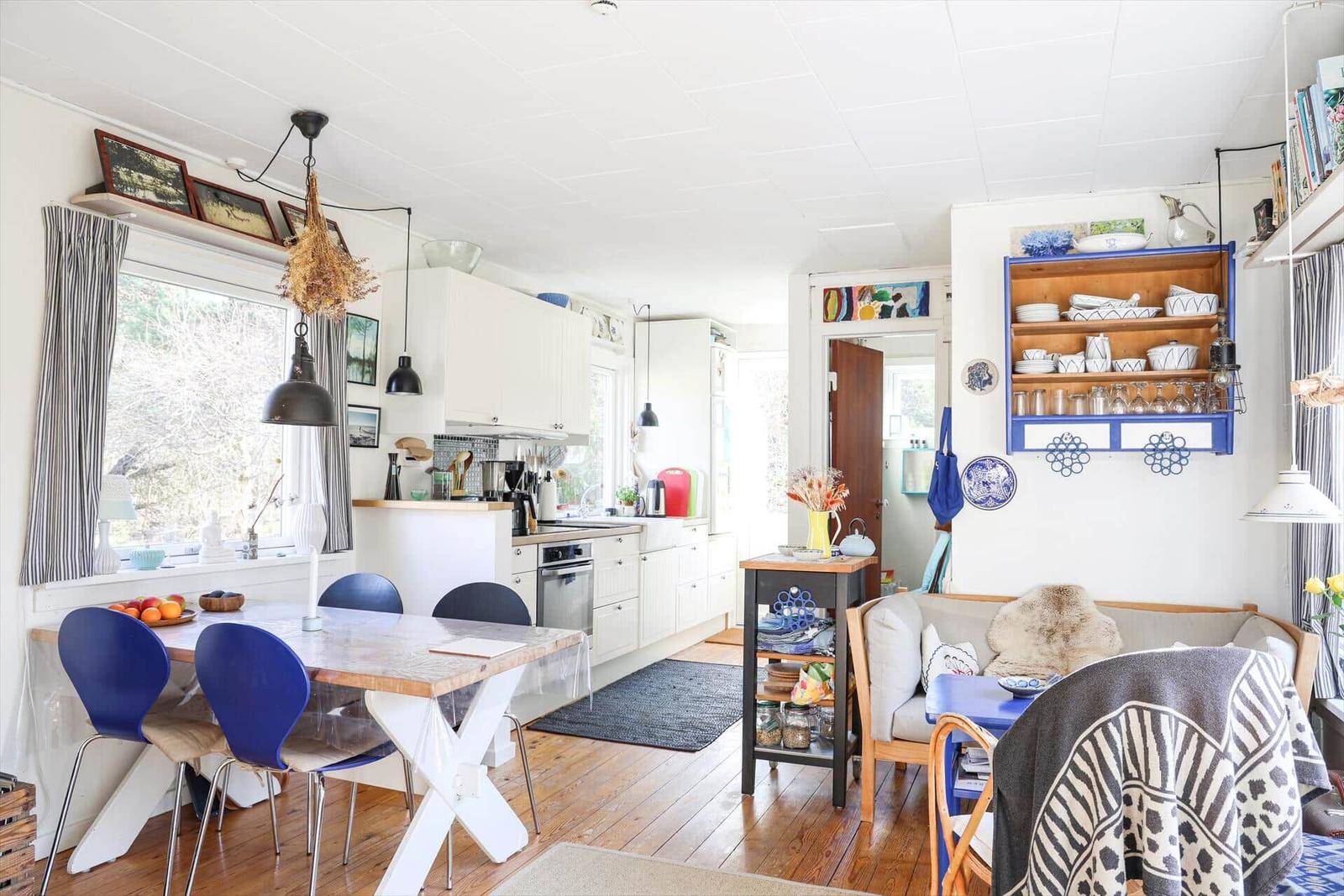 Ein Essbereich mit blauen Stühlen und einer Holzbank. Küche und Wohnzimmer sind verbunden.