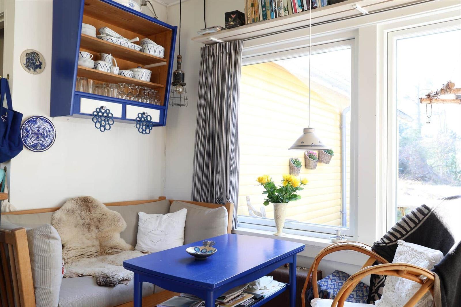 Ein Wohnzimmer mit blauem Tisch, Sofa und Schrank. Fenster mit Blumen und Vorhängen.