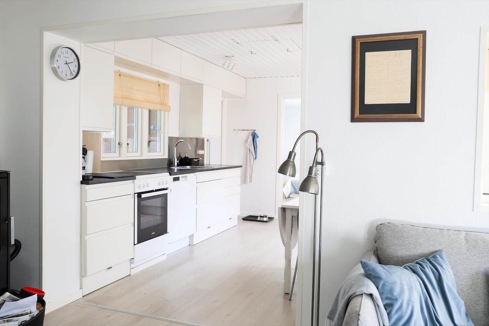 Küche mit weißen Schränken und schwarzer Arbeitsplatte. Wohnbereich mit Sofa und Stehlampe.
