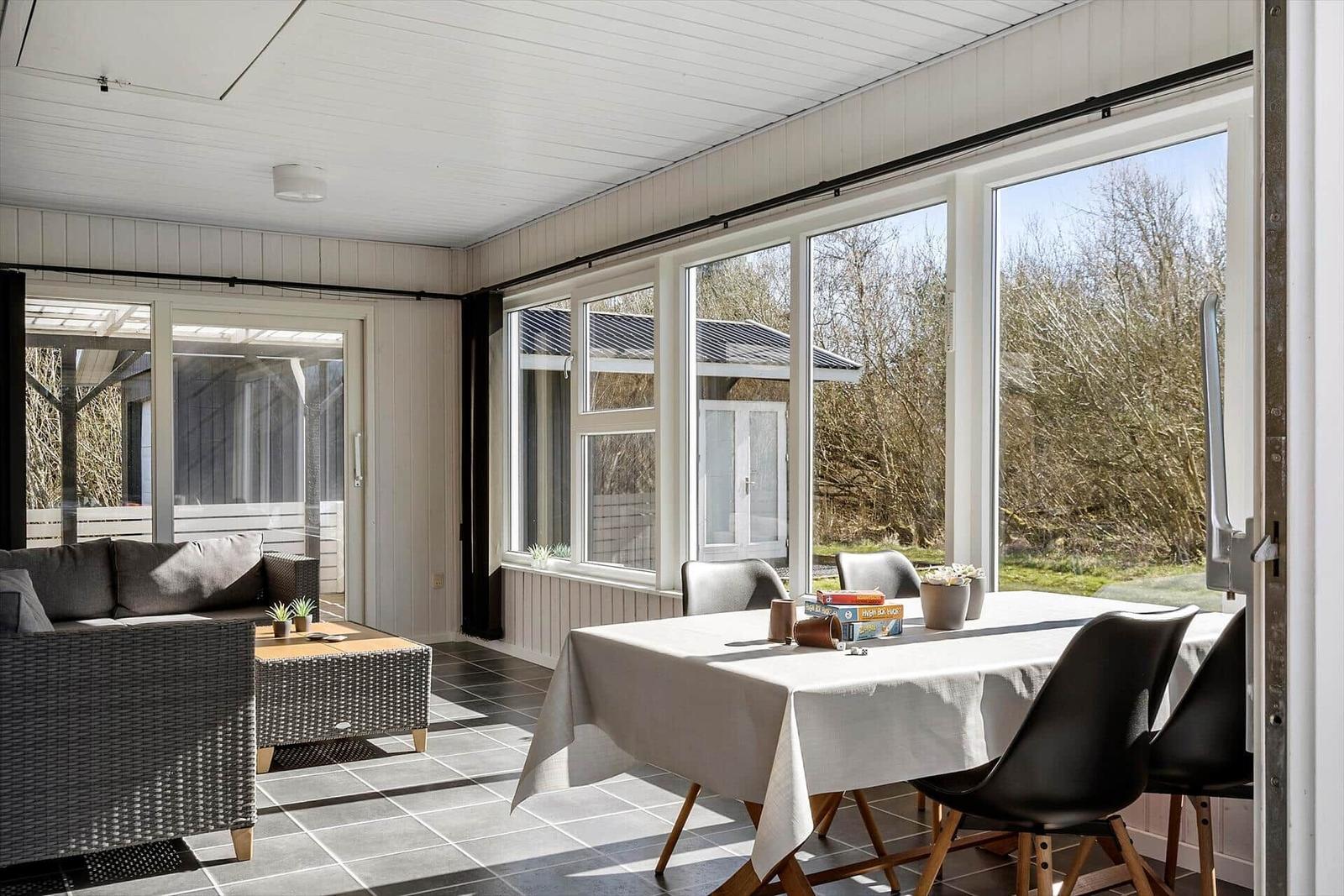 Essbereich mit Tisch und Stühlen, Wohnbereich mit Sofa und Couchtisch, große Fensterfront mit Blick auf Außenbereich.