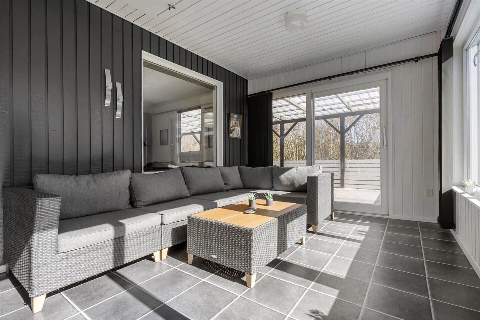 Gartenbereich mit grauem Sofa und Tisch. Durchgang zur Terrasse mit Holzgestell.