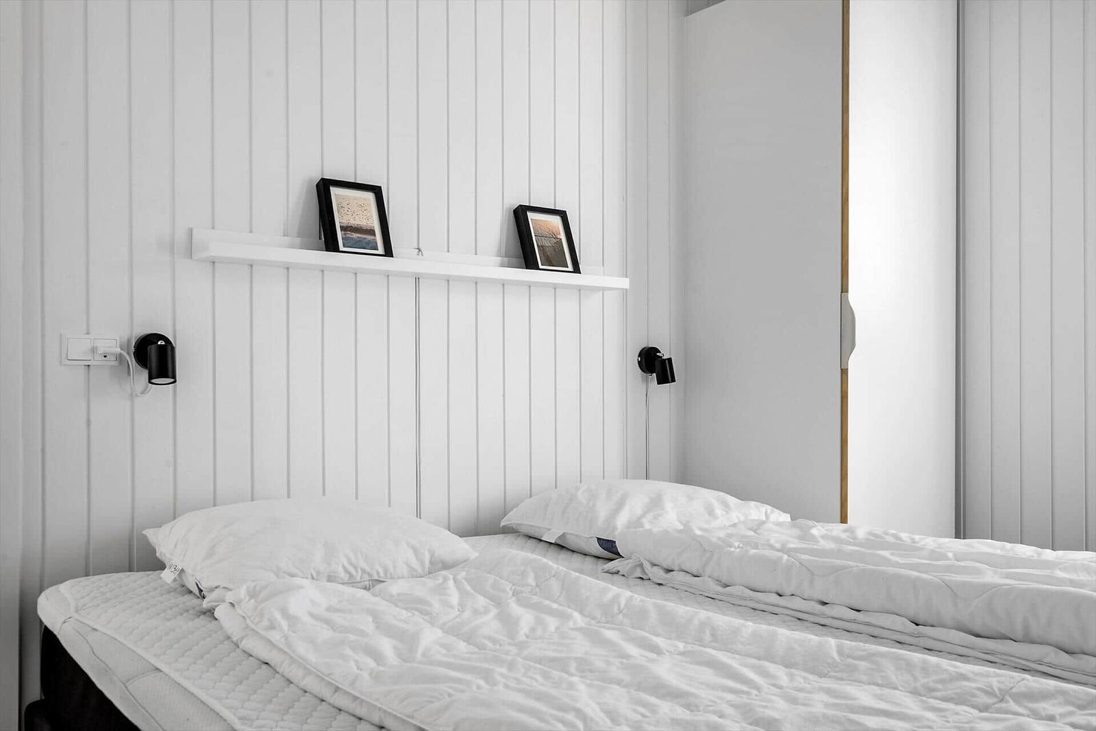 Schlafzimmer mit weißem Bett, Wandregal und schwarzen Wandlampen.