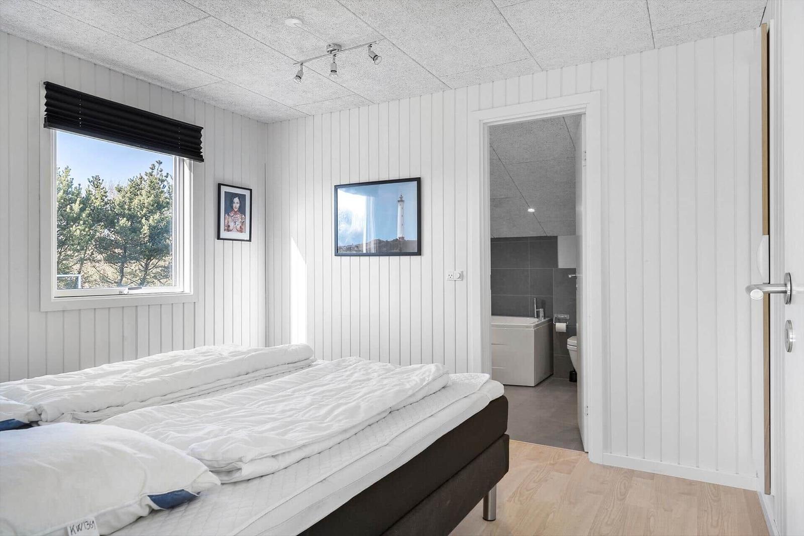 Schlafzimmer mit Bett, Fenster und angrenzender Badewanne.