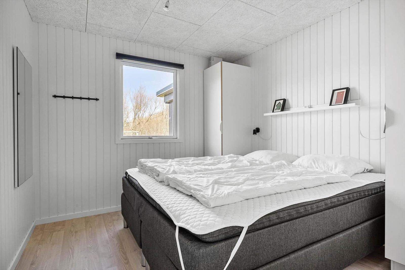 Schlafzimmer mit Bett, Fenster und Kleiderhaken an der Wand.