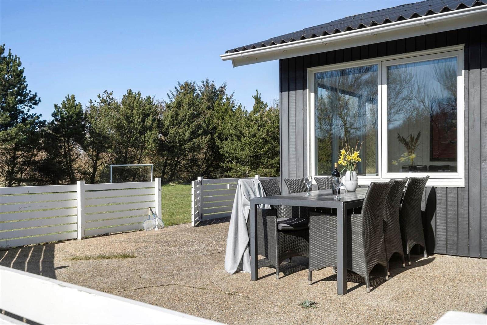 Terrasse mit Esstisch und Stühlen vor einem Haus mit großen Fenstern.