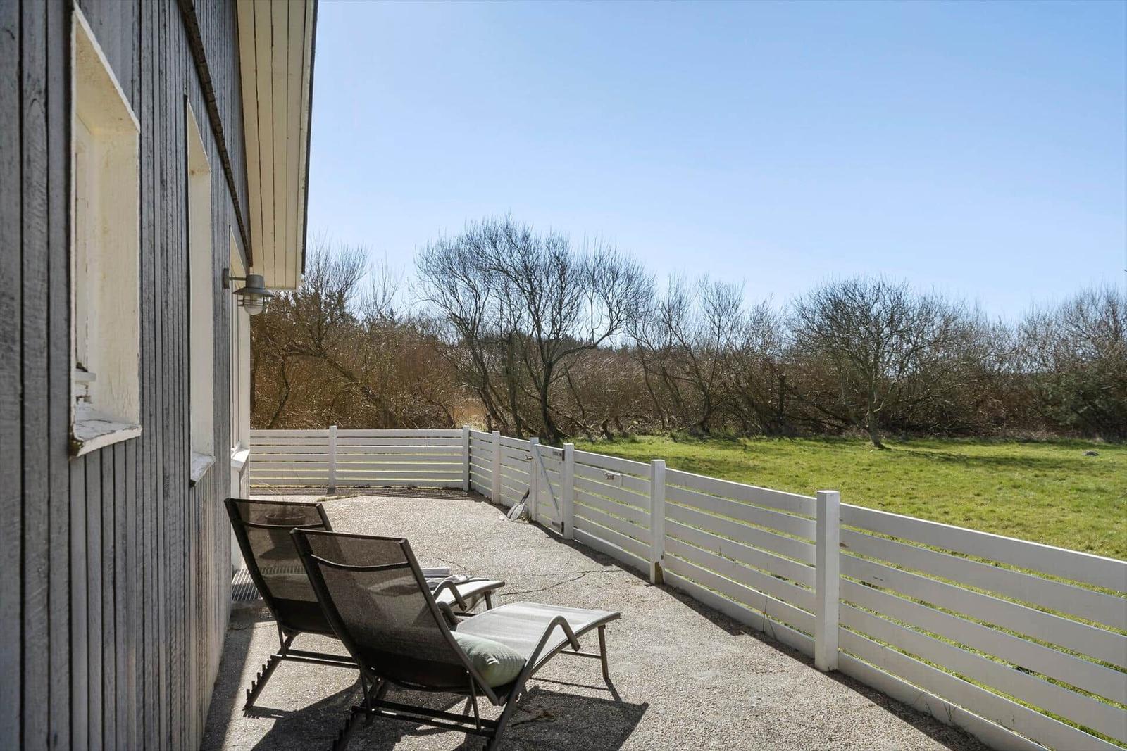 Terrasse mit Liegestühlen und weißem Zaun, Blick auf grünes Feld und Bäume.