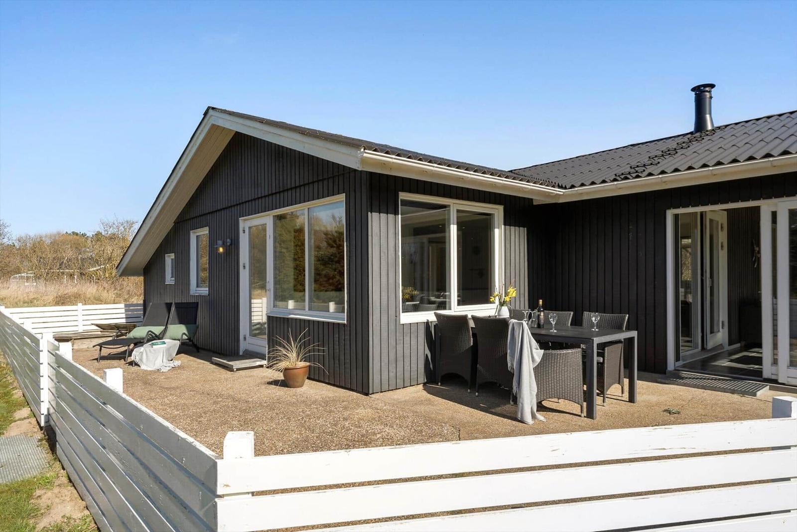Modernes Haus mit Terrasse, Gartenmöbeln und weißem Zaun.