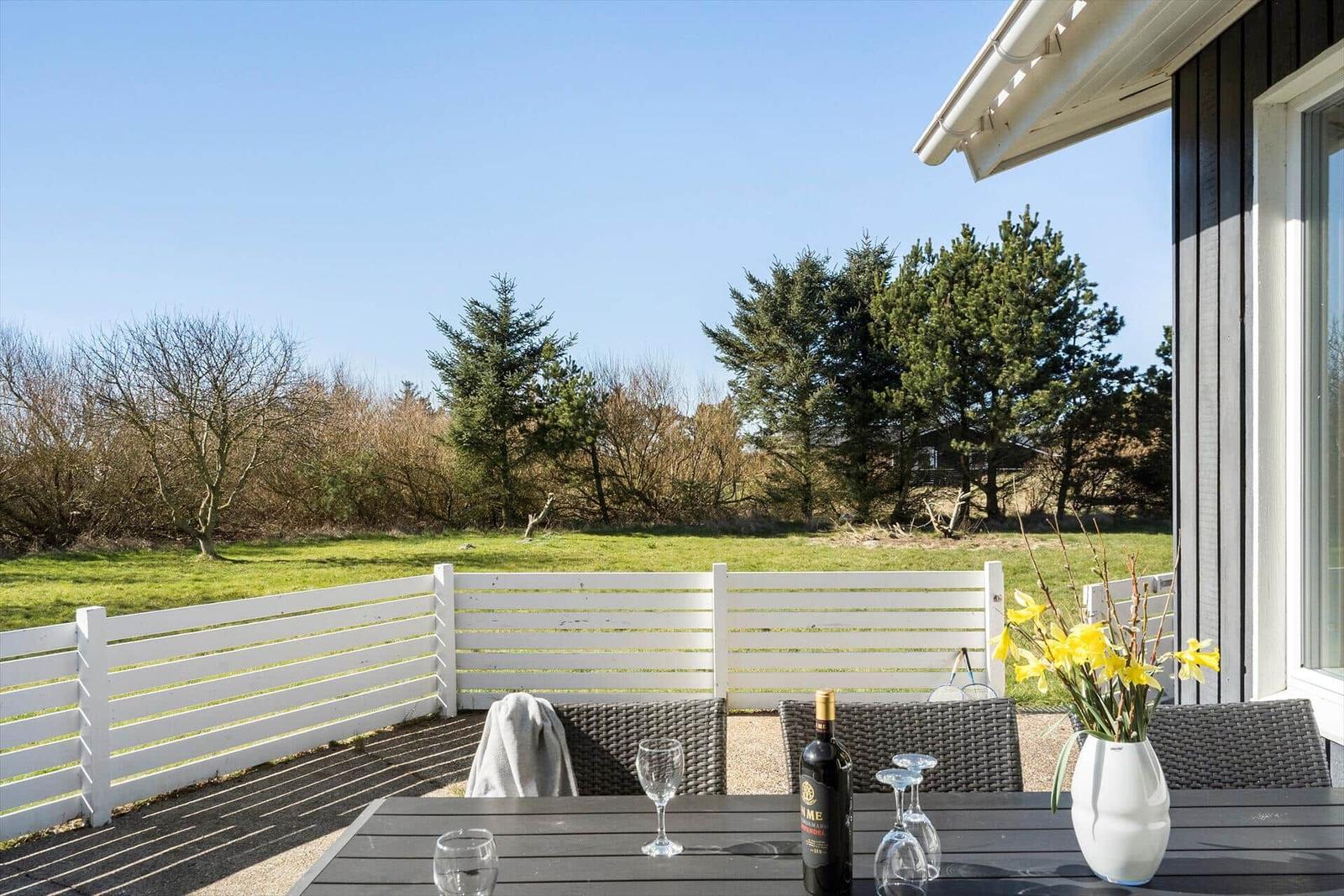 Terrasse mit Tisch, Stühlen und Blick auf Grünfläche und Bäume.