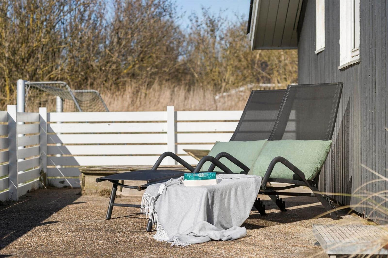 Zwei Liegestühle mit Kissen stehen auf einer Terrasse neben einem Haus.