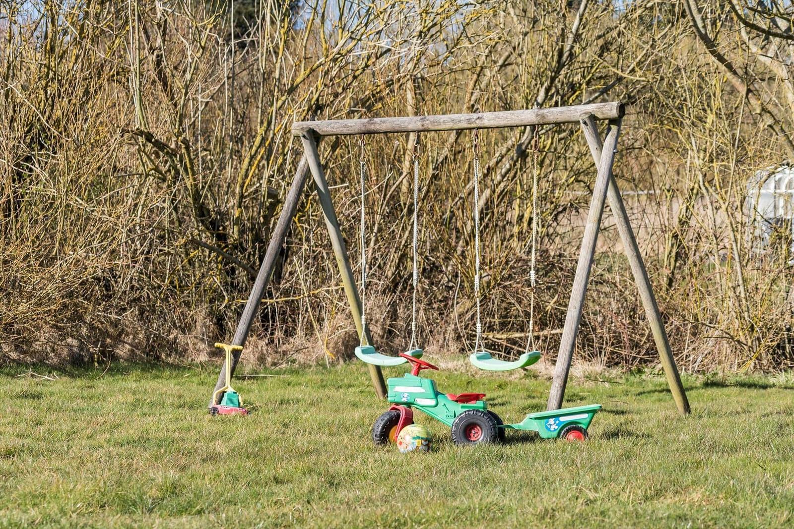 Hinterhof mit Schaukel, Spielzeugauto und Ball auf Gras.