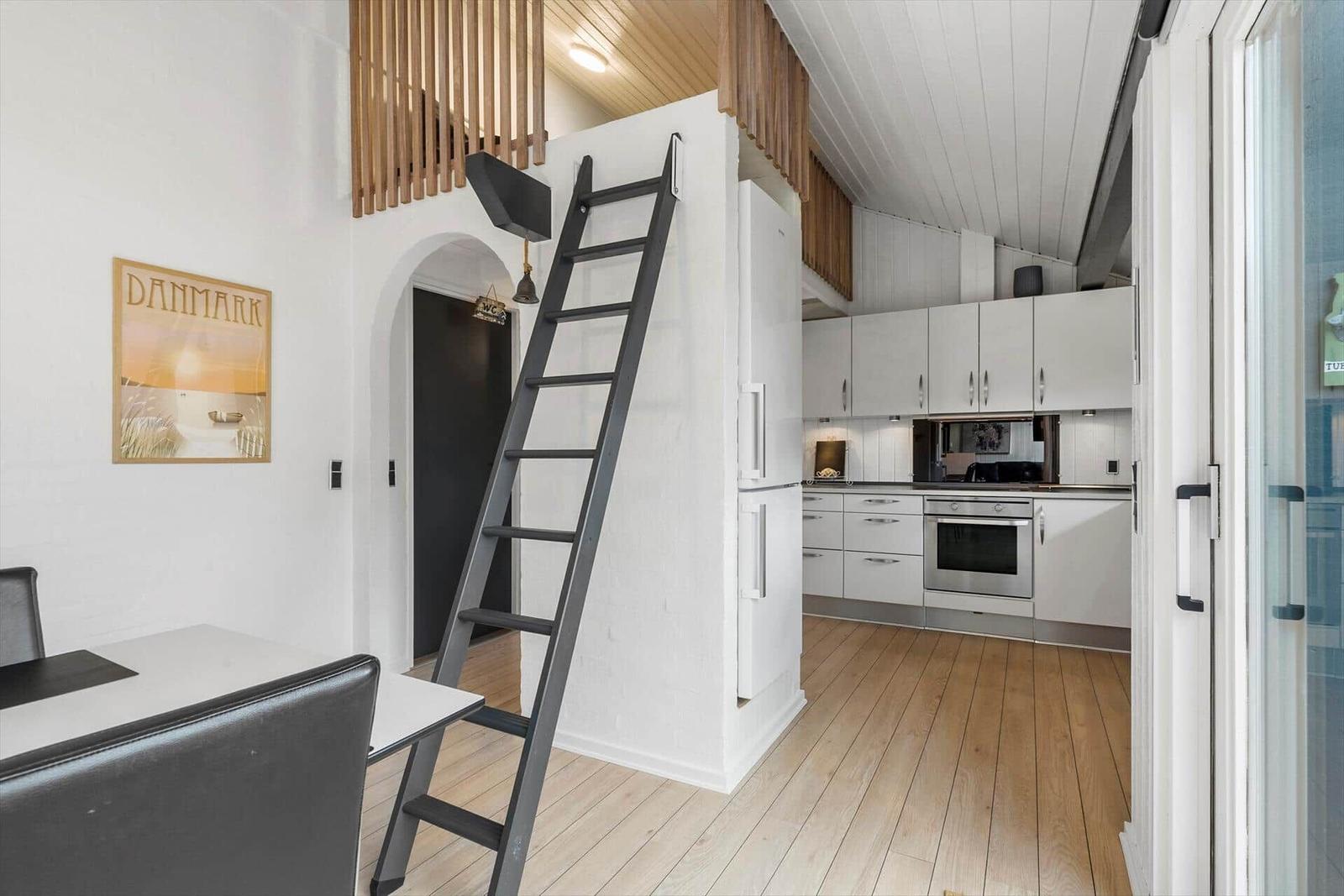 Küche mit weißen Schränken und Holzboden. Treppe führt zu einer oberen Ebene.