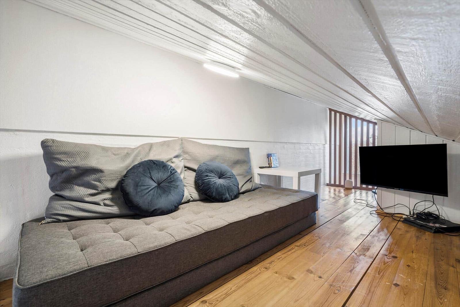 Ein Schlafzimmer mit Sofa, Fernseher und Holzboden unter einer schrägen Decke.
