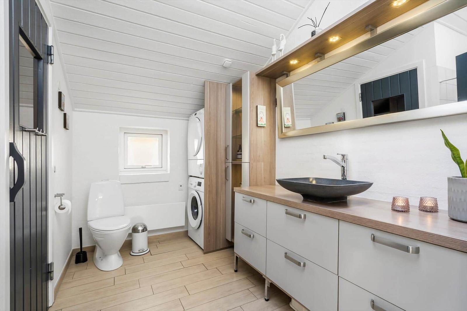Badezimmer mit Waschtisch, Spiegel, Toilette und Waschmaschine.