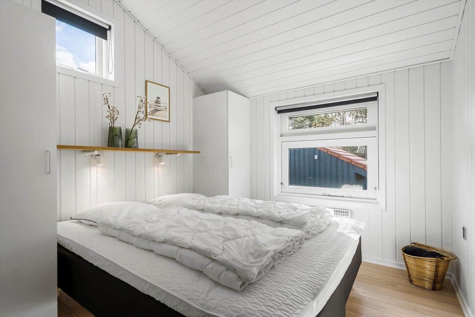 Schlafzimmer mit weißer Wandverkleidung, Bett und Fenstern.