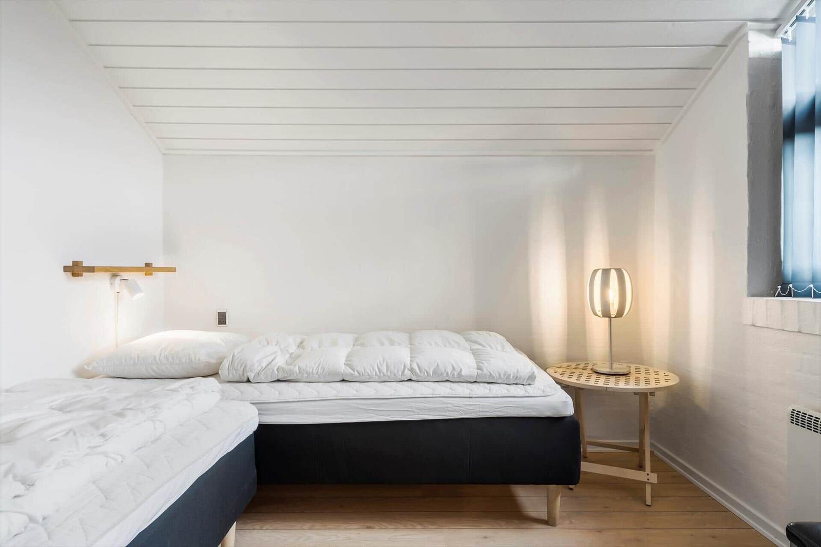Schlafzimmer mit zwei Betten, Nachttisch und Lampe. Holzdecke und Boden.