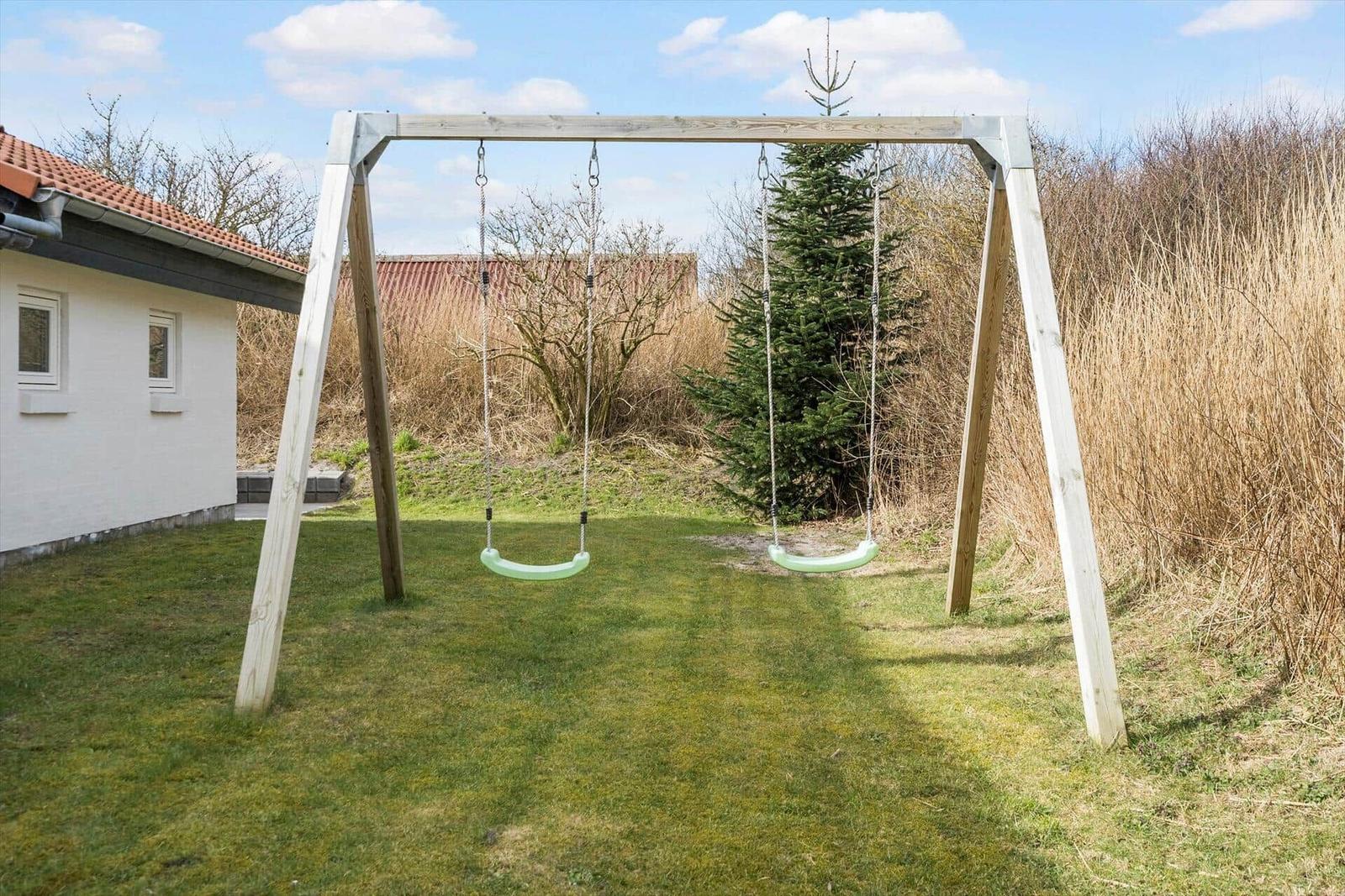 Hinter dem Haus befindet sich ein Spielplatz mit zwei Schaukeln auf einer Wiese.