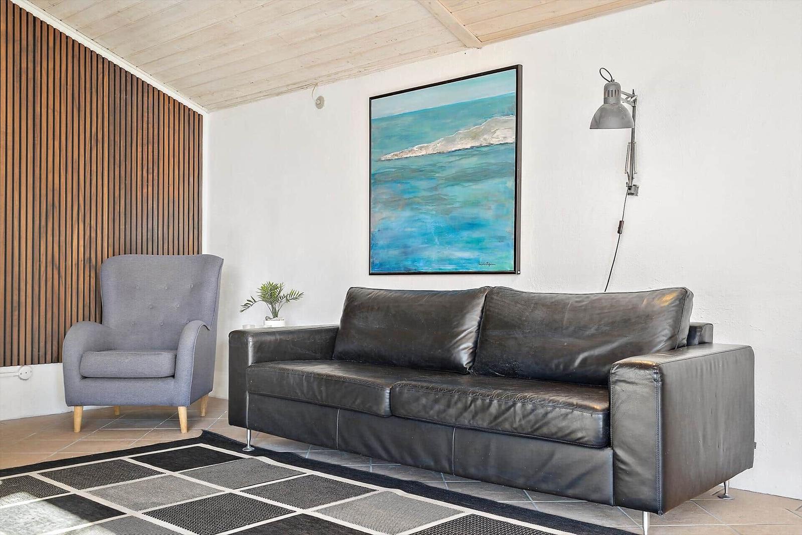 Wohnzimmer mit Ledersofa, grauer Sessel und Wandbild