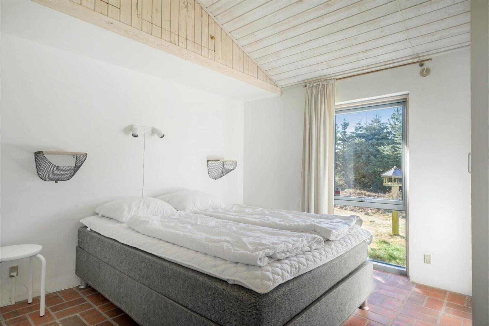 Schlafzimmer mit Bett, Fenster und Holzdecke.