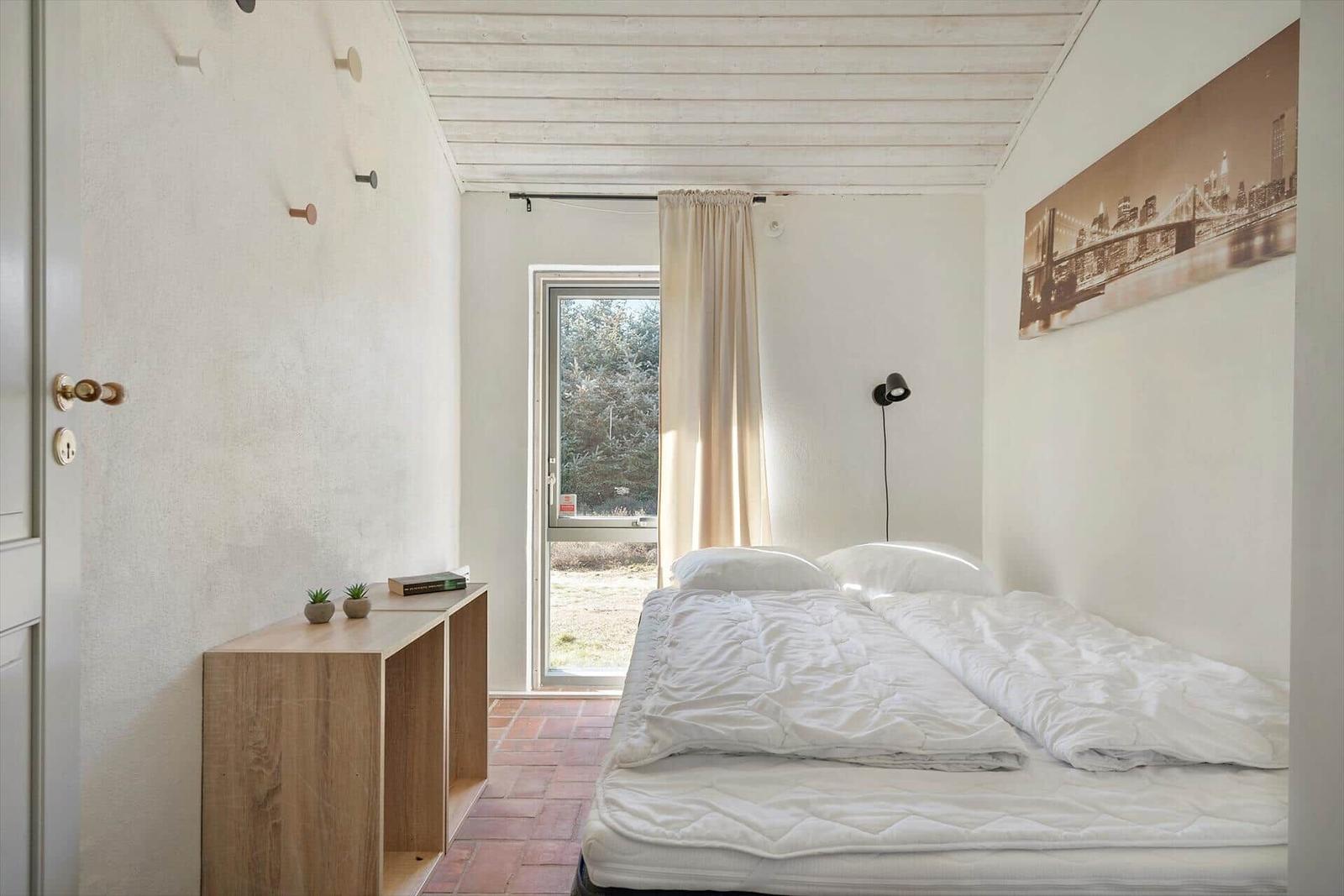 Schlafzimmer mit Bett, Fenster und Holzmöbel.