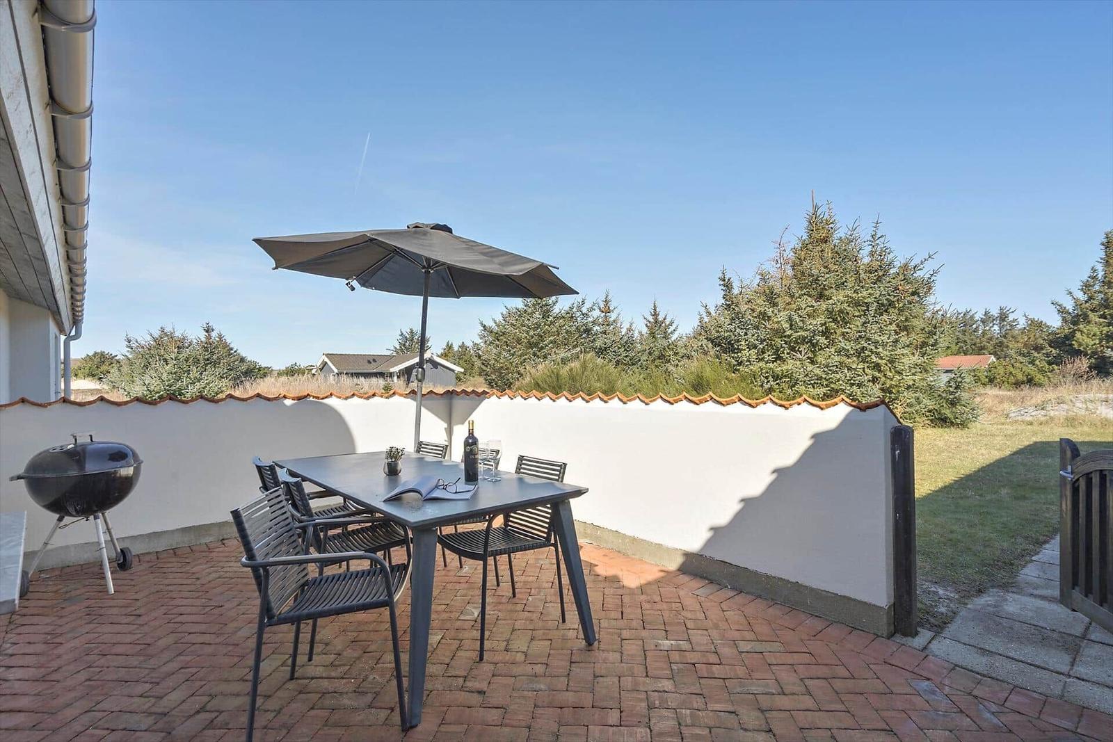Terrasse mit Tisch, Stühlen, Sonnenschirm und Grill. Hinterhof mit Grünfläche und Bäumen.
