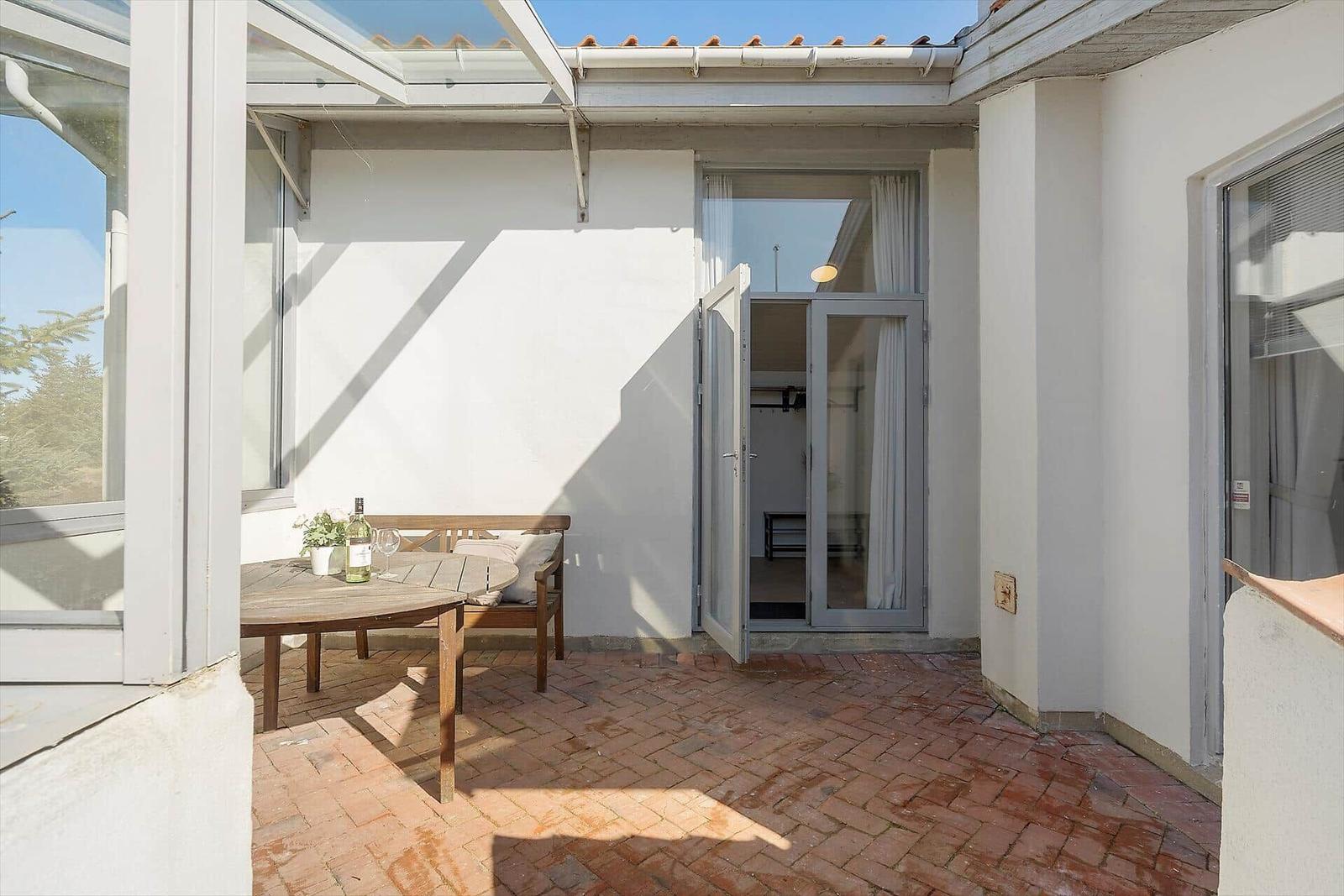 Terrasse mit Tisch, Stuhl und Flasche. Hinter dem Tisch ist eine Tür zu einem Raum.
