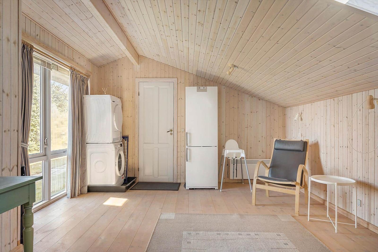 Raum mit Holzwand, Kühlschrank, Waschmaschine und Sessel.