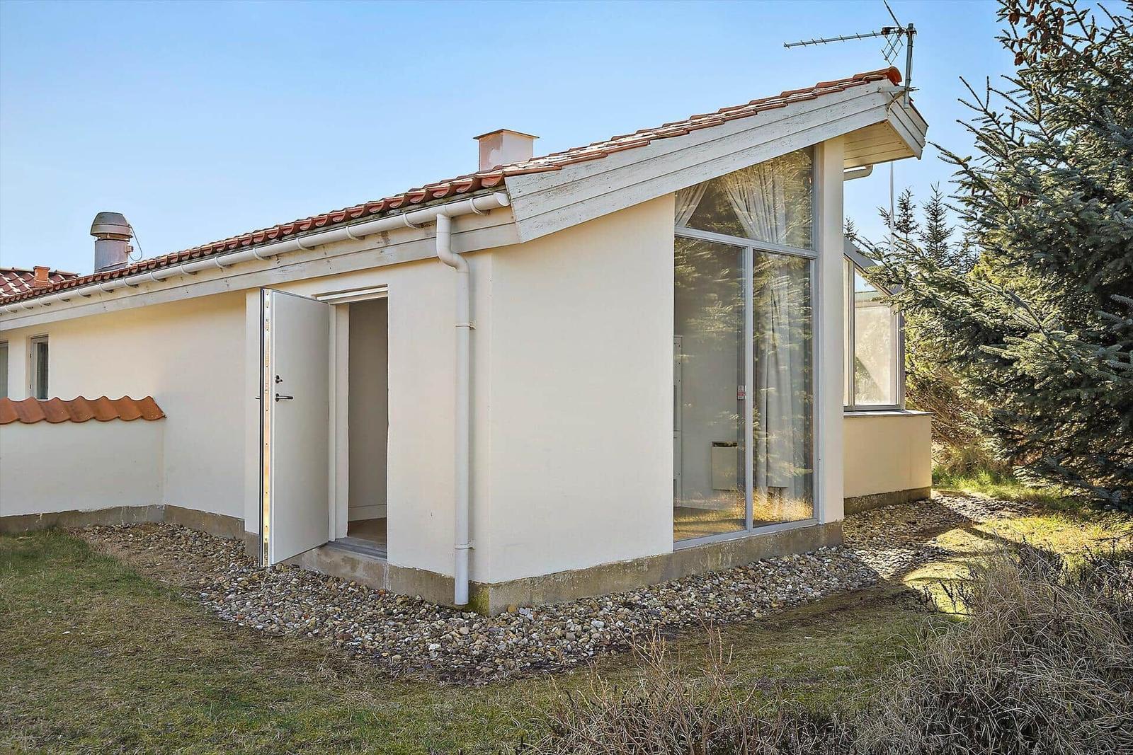 Ein modernes Haus mit Terrasse und großem Fenster. Die Fassade ist cremefarben und mit roten Ziegeln gedeckt.